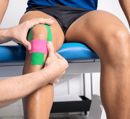 A sports physio applying green tape to a mans knee, indicating a knee injury 